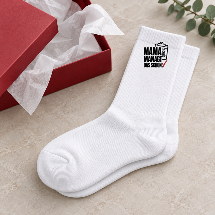 Mama managt das schon Socken als humorvolle Geschenkidee neben roter Geschenkbox