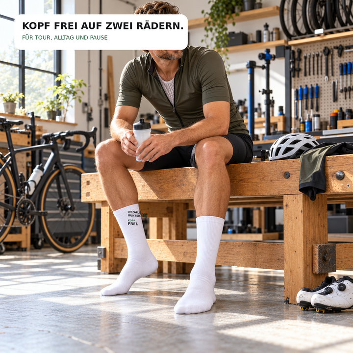 Radfahrer trägt weiße Socken mit Pedale-runter-Spruch in der Fahrradwerkstatt