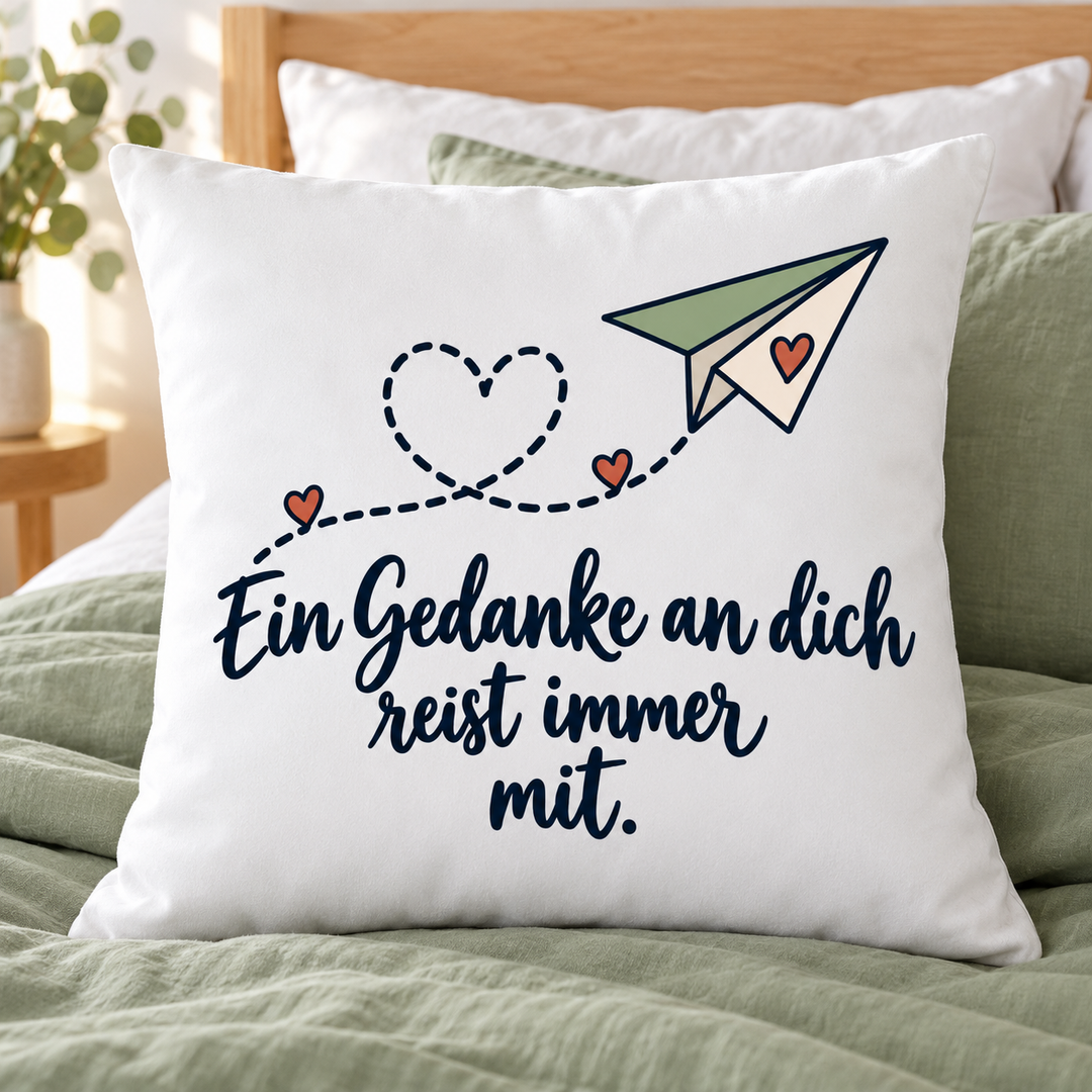 Weißes Liebeskissen „Ein Gedanke an dich reist immer mit“ auf einem Bett