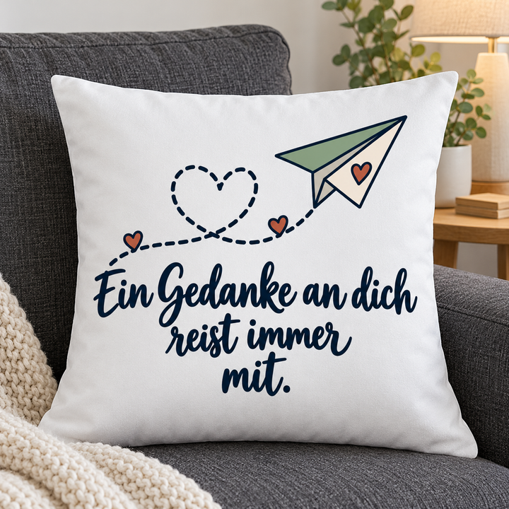 Weißes Kissen mit Papierflieger und Liebesspruch auf einem grauen Sofa