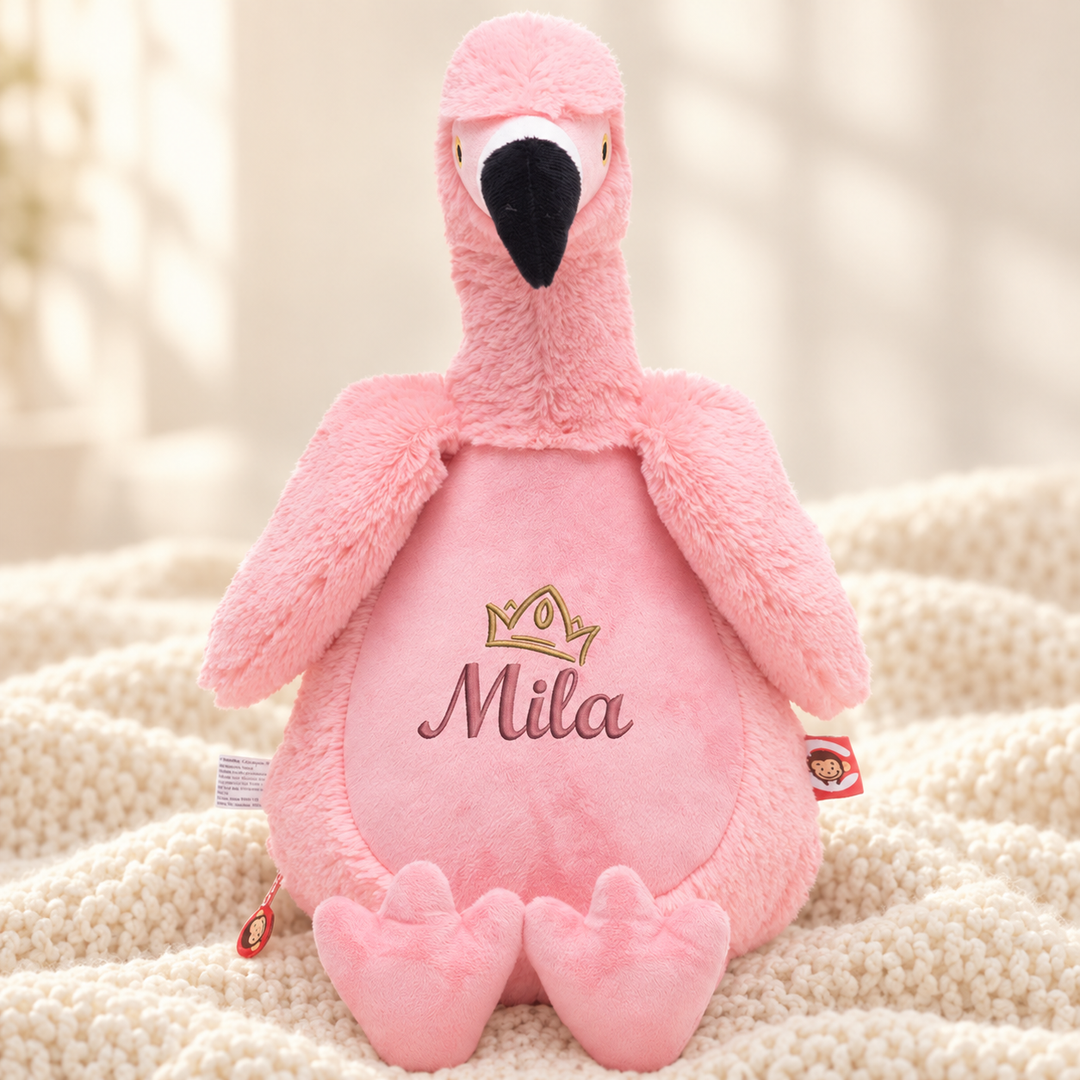 Personalisiertes Kuscheltier Flamingo mit Name & Krone – Beispiel Mila auf cremefarbener Decke