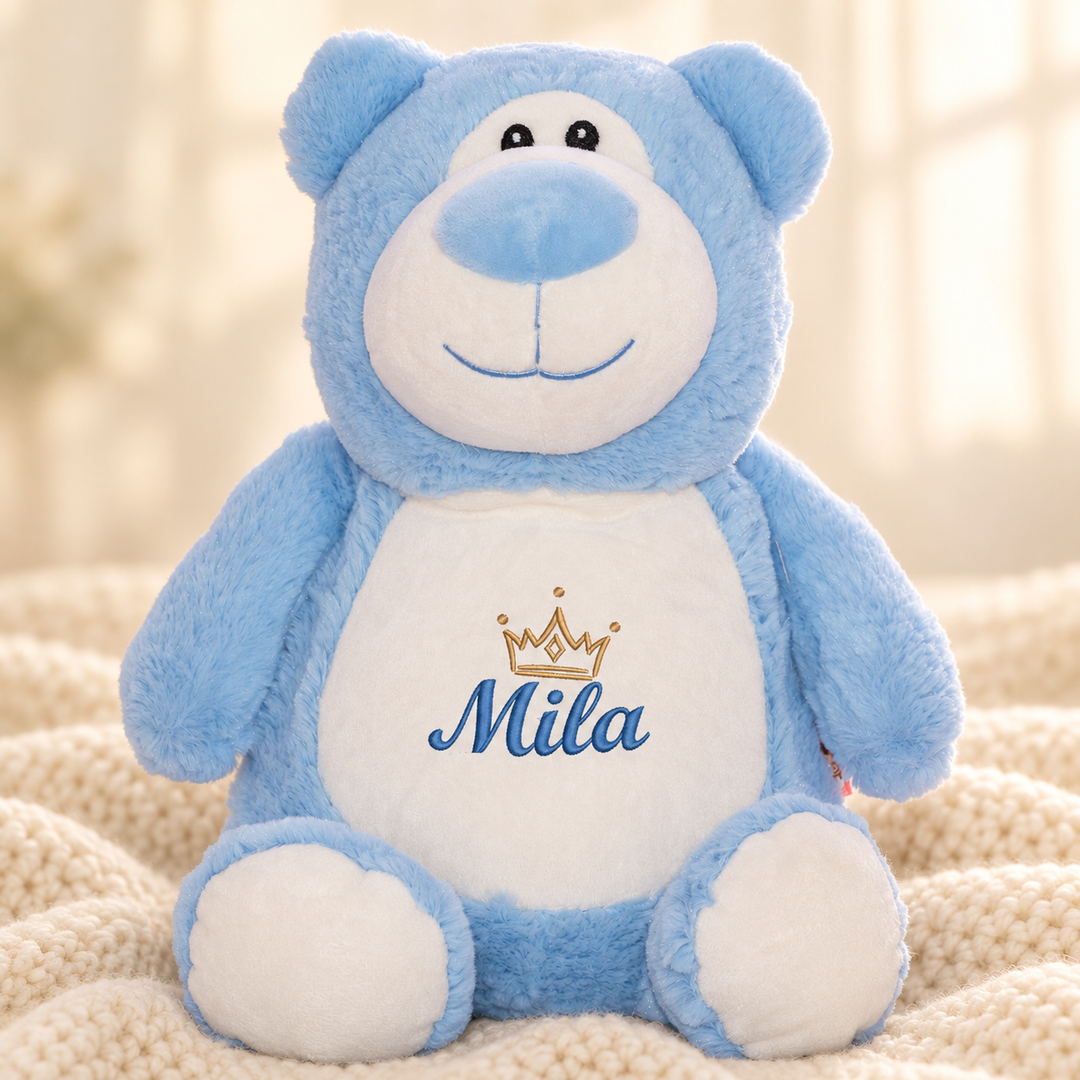 Personalisiertes Kuscheltier Bär Blau mit Name & Krone – Beispiel Mila auf cremefarbener Decke