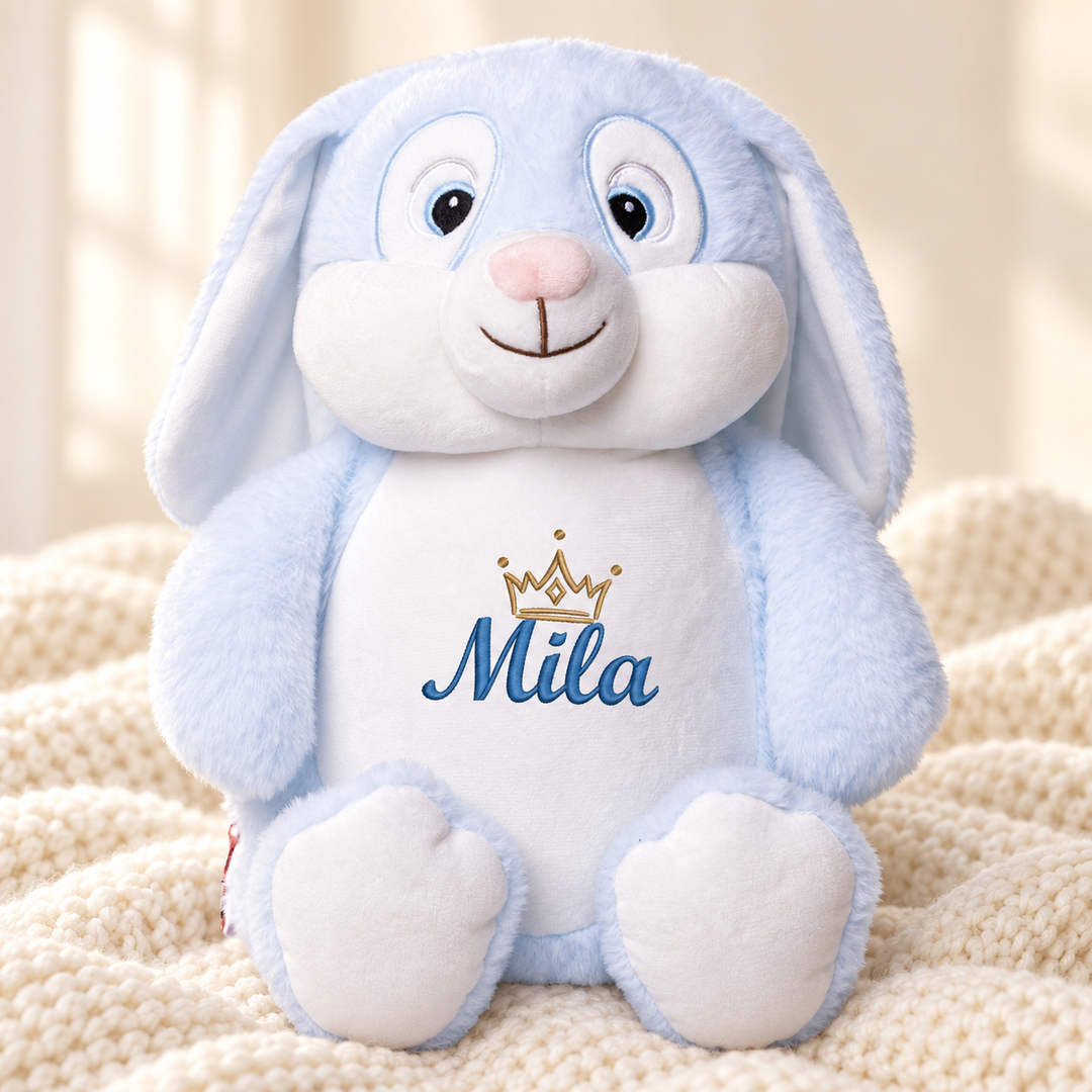Personalisiertes Kuscheltier Hase Blau mit Name & Krone – Beispiel Mila auf cremefarbener Decke