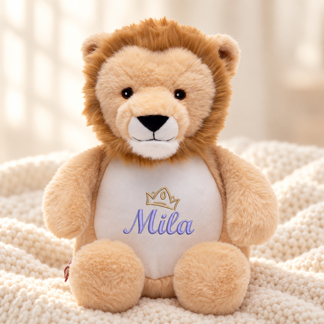 Personalisiertes Kuscheltier Löwe mit Name & Krone – Beispiel Mila auf cremefarbener Decke