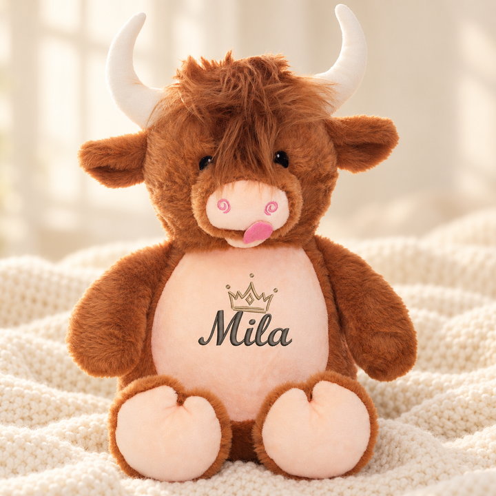 Personalisiertes Kuscheltier Highland-Kuh mit Name – Beispiel Mila auf cremefarbener Decke