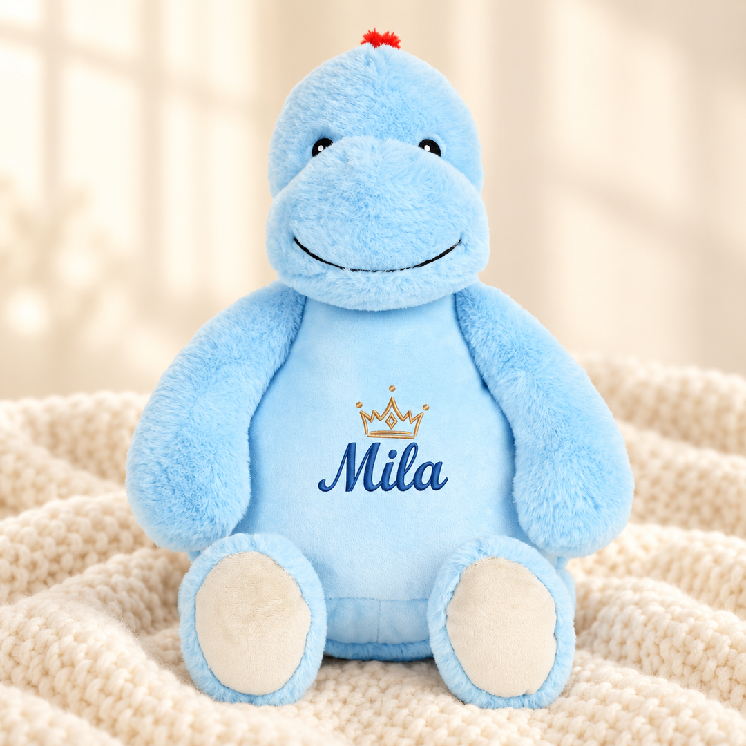 Personalisiertes Kuscheltier Dinosaurier mit Name – Beispiel Mila auf cremefarbener Decke